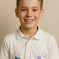 Young boy wearing a white polo shirt with logos on a beige background - showing the TeeMemento cricket motif and personalisation